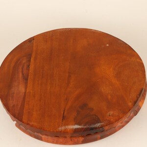 May include: A round, wooden serving tray with a rich, reddish-brown finish. The tray has a carved edge and a smooth, polished surface. The wood grain is visible, adding to its natural aesthetic. The tray is ideal for serving food or displaying decorative items.