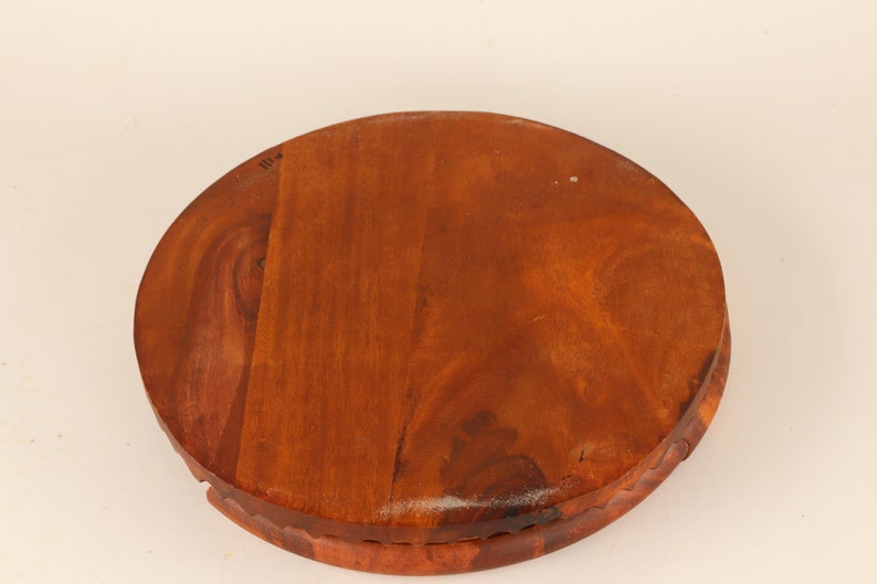 May include: A round, wooden serving tray with a rich, reddish-brown finish. The tray has a carved edge and a smooth, polished surface. The wood grain is visible, adding to its natural aesthetic. The tray is ideal for serving food or displaying decorative items.