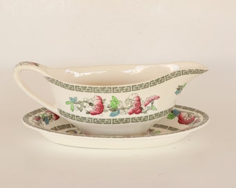 May include: A white porcelain gravy boat with a green and floral design. The boat is on a matching saucer.