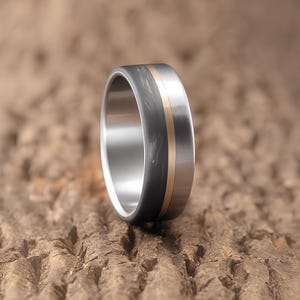 Men's anniversary gift ring in gunmetal carbon fiber, titanium, and brass, close up on warm neutral background