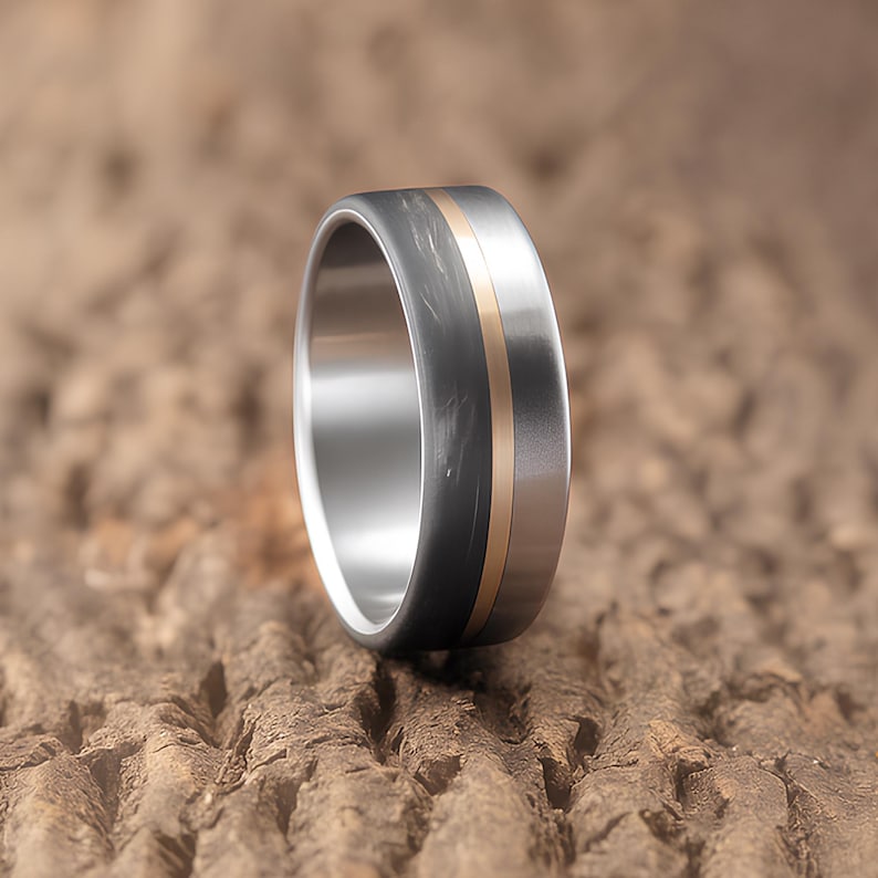Men's anniversary gift ring in gunmetal carbon fiber, titanium, and brass, close up on warm neutral background