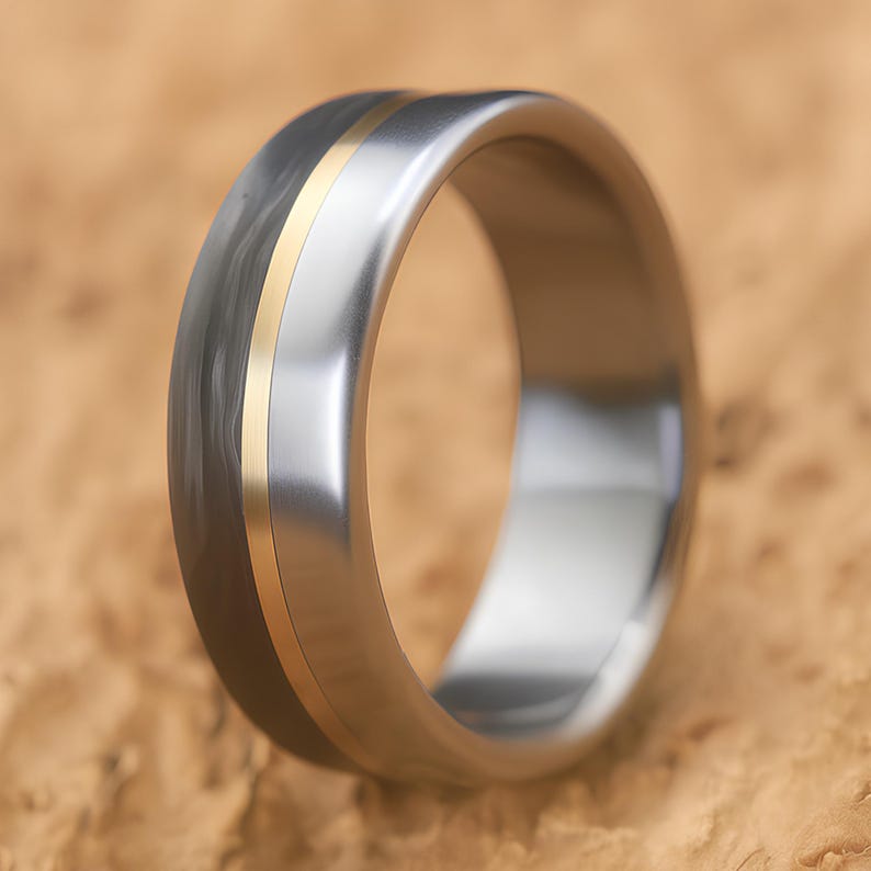 Modern men's engagement ring in titanium and carbon fiber with brass accent, standing on tan stone surface