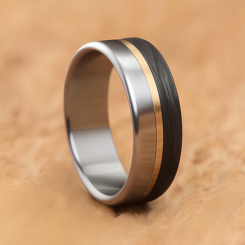 Titanium carbon fiber men's wedding band with brass inlay stripe standing upright on a sandstone background