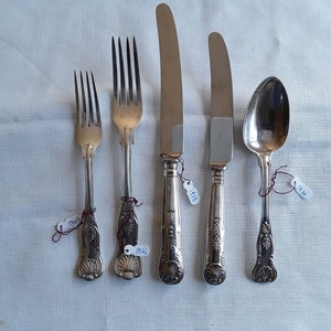 May include: A set of five silver-plated cutlery pieces, including two forks, two knives, and a spoon. Each piece features an ornate design and is labelled with a year, ranging from 1932 to 1945.