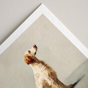 May include: A print of a dog with cream and brown fur, looking upwards. The dog is positioned on a light gray background, with a white border around the print. The dog's fur has a textured appearance, and the artwork has a vintage aesthetic.