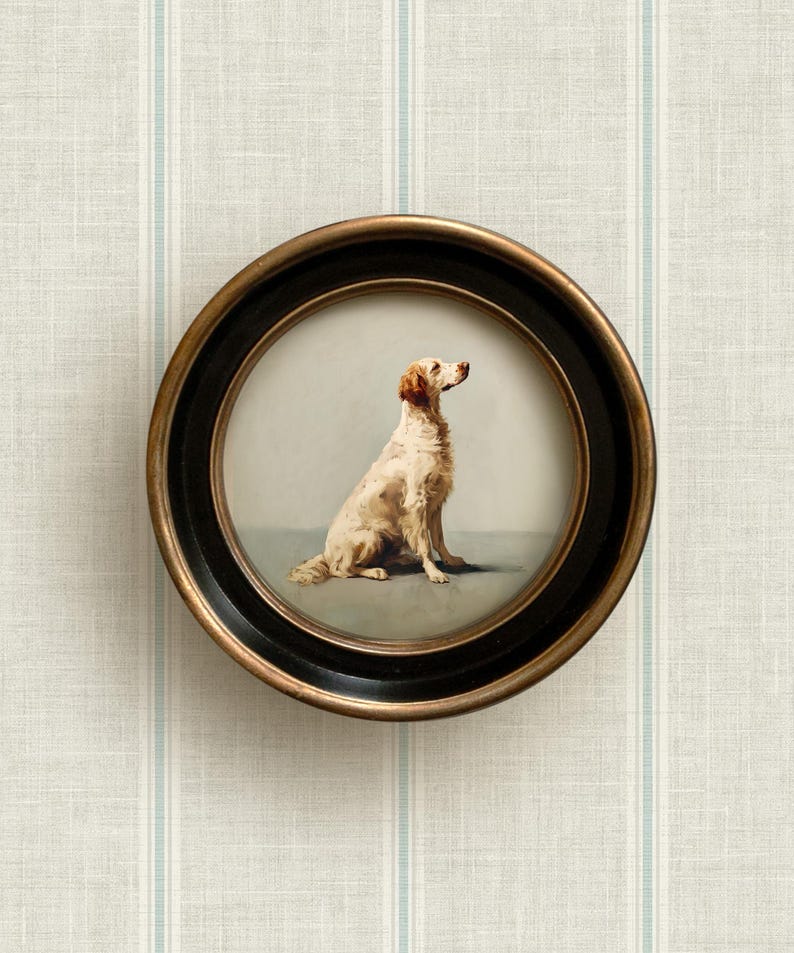 May include: A round framed dog portrait. The artwork features a seated dog with a light brown and white coat, set against a soft gray background. The frame is black with a gold-colored inner rim. The artwork is displayed against a striped wallpaper.