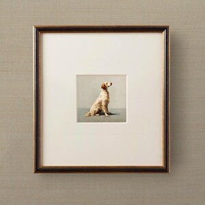 May include: Framed artwork featuring a seated dog with light brown fur, set against a muted gray background. The artwork is matted in white and framed in a dark brown frame with a gold inner edge. The frame is displayed on a textured, neutral-toned wall.