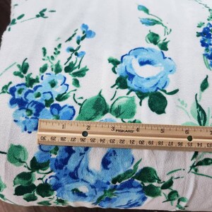 May include: White fabric with a blue and green floral pattern. The fabric is folded and a ruler is placed on top of it. The ruler is marked with inches.
