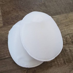 May include: Two white oval-shaped bra pads with a white stitched edge.
