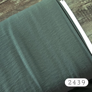 May include: A bolt of dark sage green fabric with a fine, subtle ribbed texture. The material is rolled tightly, showing a consistent matte finish across the surface. A white rectangular label with the black printed number 2439 is visible.