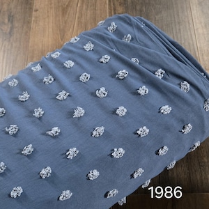 May include: A close-up of a blue fabric with white polka dots. The fabric has a textured, puffy look. The number 1986 is printed in white on the bottom right corner of the image.