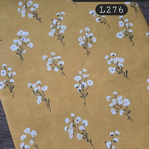 May include: A mustard yellow fabric featuring a repeating pattern of small white flowers with dark stems. The text 70/30, cotton/linen, and L276 is printed in black boxes on the upper right side of the textile, indicating the material composition.