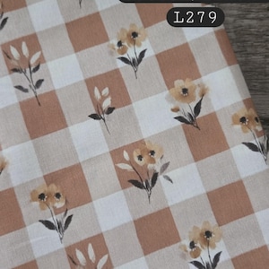 May include: A fabric featuring a tan and white gingham check pattern with small printed yellow flowers and green stems. The text 70/30, cotton/linen, and L279 is printed in the upper right corner of the fabric.