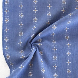 May include: Blue fabric with a white and orange floral pattern. The fabric has a textured surface and is folded in half.
