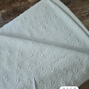 May include: Folded light blue fabric with a textured, dotted pattern. The fabric has a soft appearance and is likely used for clothing or home decor. The number "2357" is printed on the fabric.