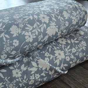 May include: A close-up of a blue fabric with a white floral pattern. The fabric is folded in half and has a ribbed texture.