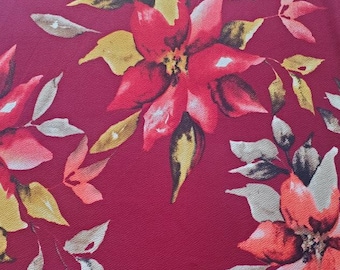 May include: A close-up of a fabric with a burgundy background and a floral pattern. The flowers are red with orange and white accents. The leaves are yellow, brown, and gray.
