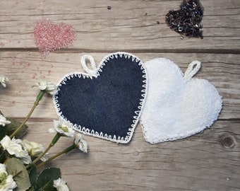 May include: Two heart-shaped kitchen scrubbers, one blue denim and one white terry cloth, with white crocheted trim. The scrubbers are on a wooden surface.