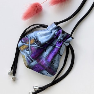 Könnte beinhalten: Eine kleine, blaue Kordeltasche mit einem abstrakten Design in Lila und Gelb. Die Tasche hat schwarze Kordeln mit silbernen Metallspitzen.
