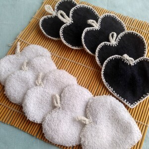 Op de afbeelding: Twee sets hartvormige herbruikbare make-up remover pads. De ene set is wit en de andere is zwart. Beide sets zijn afgewerkt met wit haakwerk.