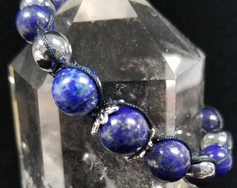 Pode incluir: Um bracelete de contas azuis e prateadas com um cordão preto. O bracelete é feito com contas de lapis-lazúli e hematita.