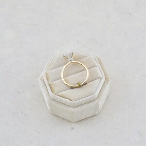 Puede incluir: Un anillo de oro con una gema transparente de talla brillante redonda en un engaste de garras. La banda es fina y de oro pulido, y el engaste incluye un peque&ntilde;o grupo de diminutas piedras de acento visibles bajo la piedra central.