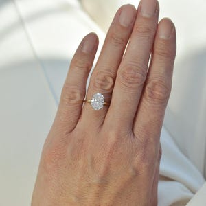 Puede incluir: Un anillo de oro con una piedra preciosa transparente de corte ovalado en un engaste de cuatro garras. La banda es fina y pulida, con un acabado amarillo met&aacute;lico. La piedra preciosa est&aacute; situada en el centro y refleja la luz con facetas.