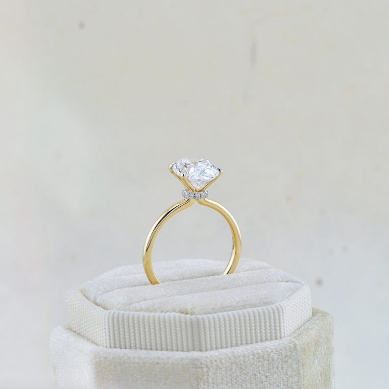 Puede incluir: Un anillo de oro con una piedra central grande, transparente y facetada en un engaste de garras. Una banda delgada de peque&ntilde;as piedras pav&eacute; transparentes rodea la base del engaste de la piedra central, aportando un brillo sutil bajo la gema.