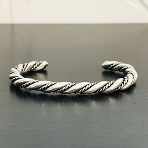 May include: A silver twisted bangle bracelet. The bracelet is made of a thick, twisted wire.