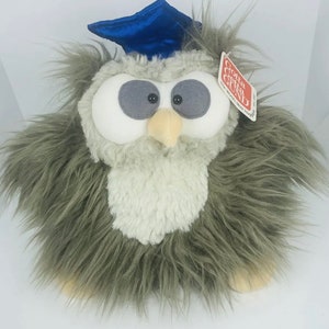 Puede incluir: Un juguete de peluche de búho con pelaje gris y un gorro de graduación azul. Tiene ojos grises grandes, un pecho blanco y un pico amarillo. Una etiqueta dice "Gotta Getta Gund".