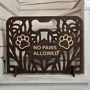 Pode incluir: Um portão de madeira marrom para animais de estimação com um design de impressão de pata e o texto "NO PAWS ALLOWED".