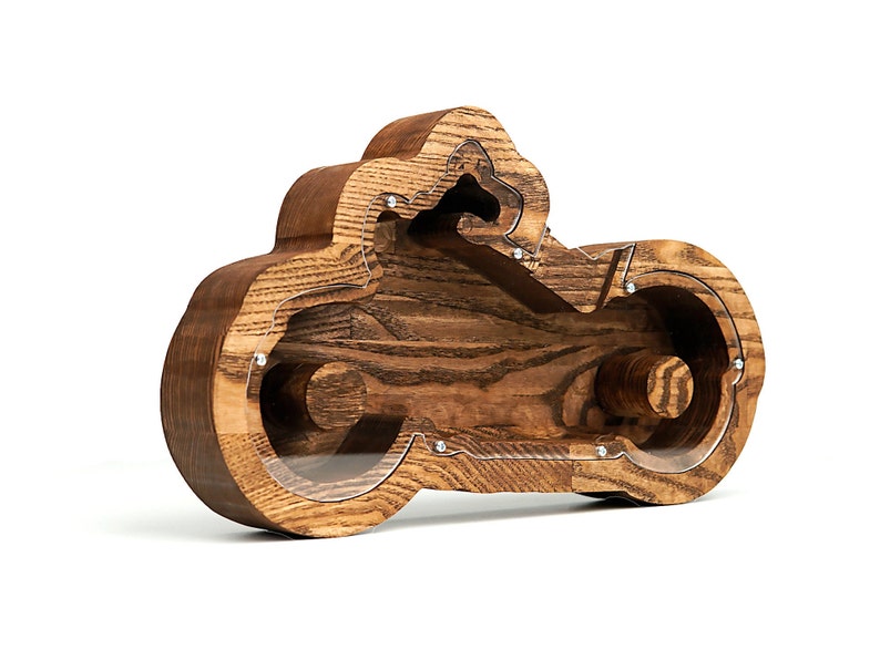 May include: Wooden motorcycle shaped piggy bank with a clear acrylic window. The bank is made of dark brown wood with a natural wood grain.