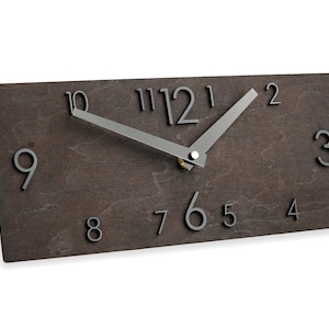 Peut inclure: Une horloge rectangulaire en bois brun avec des chiffres noirs et des aiguilles argentées. Le cadran de l'horloge comporte les chiffres de 1 à 12.