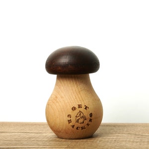 Könnte beinhalten: Ein hölzerner Behälter in Pilzform mit einem dunkelbraunen Deckel und einem hellbraunen Körper. Der Behälter trägt die Gravur "Get Crackin'" an der Seite.