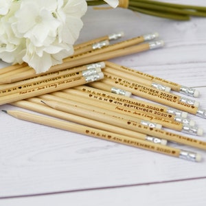 Puede incluir: Un montón de lápices de madera con gomas blancas. Los lápices están grabados con el texto "M&M 4TH SEPTEMBER 2020" y "Pencil us in Jacob & Emily 20th June 2020".