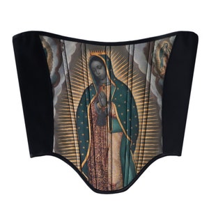 May include: A black corset with a colorful image of the Virgin Mary printed on the front. The image is surrounded by a gold halo and rays of light.