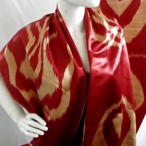 May include: A red and gold silk scarf with an ikat pattern. The scarf is draped around a white mannequin.