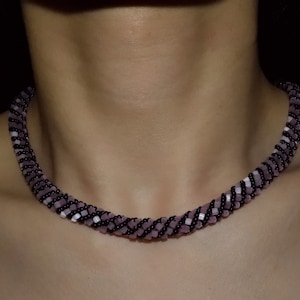May include: A close-up of a black and purple beaded necklace worn around a person's neck.