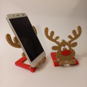May include: Two phone stands made of brown wood, shaped like reindeer. One stand is red and the other is brown. Both stands have a slot to hold a phone.
