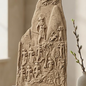 Puede incluir: Un relieve de piedra tallada de color beige que representa una escena de batalla con figuras y símbolos. El relieve está montado sobre una base rectangular de color claro. La obra de arte presenta tallas detalladas de guerreros.
