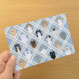 May include: A blue card with a repeating pattern of cat illustrations. Each cat has a unique appearance, with different colours and patterns. The background features a diamond lattice design with floral accents. The card is held by a hand.