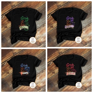 May include: Four black t-shirts with a graphic of the Sorting Hat from the Harry Potter series. Each shirt features a different Hogwarts house: Gryffindor, Hufflepuff, Slytherin, and Ravenclaw.