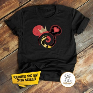 K&ouml;nnte beinhalten: Schwarzes T-Shirt mit einem roten und gelben Mickey-Maus-Kopfdesign mit einer Krone, Herzen und einem Spiralmuster. Der Text "PERSONALISIERE DEIN SHIRT OPTION VERF&Uuml;GBAR!" befindet sich auf einem gelben Banner in der linken unteren Ecke. Der Text "Harlequin's Handmade" befindet sich auf einem braunen Kreis in der rechten unteren Ecke.