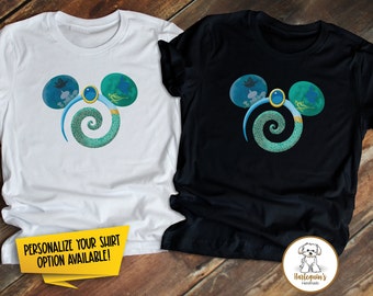 May include: Two t-shirts with a blue and green Mickey Mouse ear design featuring a genie lamp, magic carpet, and a swirl. The text "PERSONALIZE YOUR SHIRT OPTION AVAILABLE!" is on the white t-shirt.