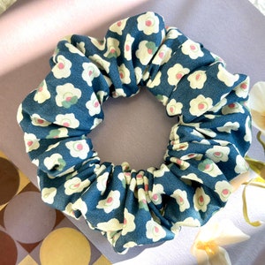 May include: A blue and white scrunchie with a floral pattern. The flowers are white with a pink centre and green leaves.