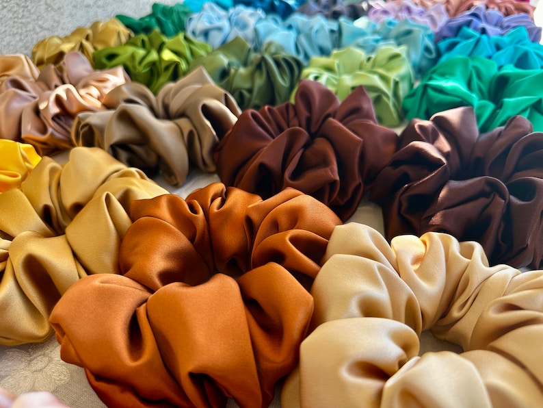 May include: A collection of colourful satin scrunchies in various shades of brown, beige, and green. The scrunchies are made of soft, silky fabric and are perfect for adding a touch of style to any hairstyle.