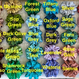 May include: A collection of 40 scrunchies in various colours and fabrics, including beige, white, yellow, brown, green, blue, purple, pink, red, and black. The scrunchies are arranged in a grid pattern and labelled with their corresponding colour names.
