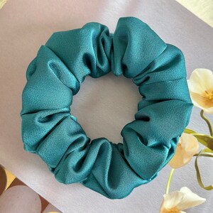 May include: Teal blue satin scrunchie hair tie. The scrunchie is made of soft, smooth fabric and is perfect for holding hair in place.