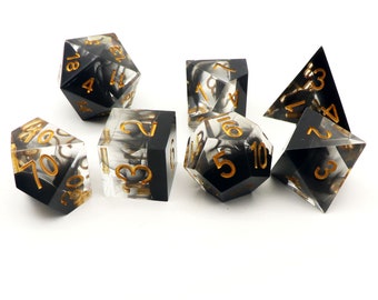 May include: Set of seven black and white dice with gold numbers. The dice are made of clear acrylic with a black swirl pattern. The numbers are visible on each side of the dice.