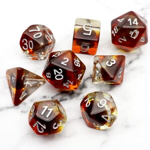 May include: Set of eight brown and clear dice with white numbers. The dice are translucent and have a swirling pattern inside. The numbers on the dice are 2, 3, 4, 5, 6, 8, 11, 12, 14, 18, 20, 30, 70.